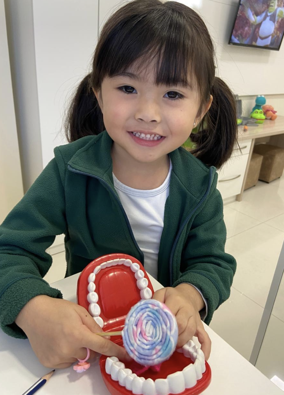 Menina sorrindo com modelo de arcada dentária durante orientação de escovação
